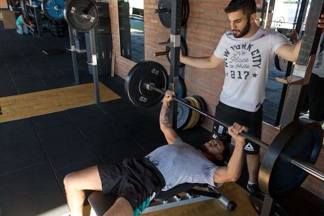 A man doing a bench press with his trainer spotting him